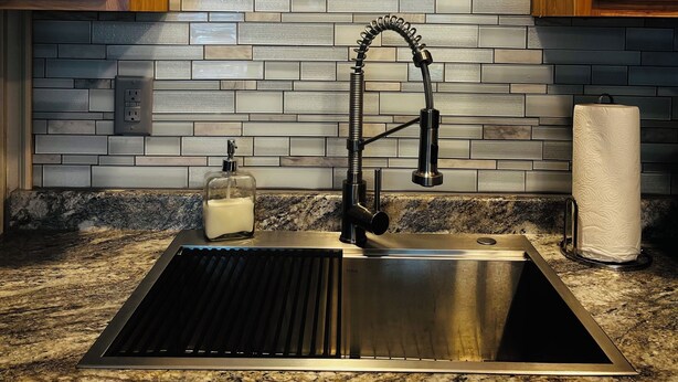 A kitchen with a stainless steel sink, wooden cabinets, a round backsplash with a decorative plate, and a granite countertop. - Adorable 2 Bedroom Unit with Boat Parking (Dauphin Island)