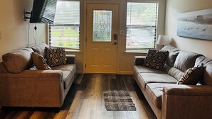 A living room with two sofas, a flat-screen TV mounted on the wall, and a door with a glass window. - Adorable 2 Bedroom Unit with Boat Parking (Dauphin Island)