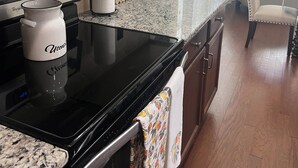 Een moderne keuken met een zwart fornuis, een roestvrijstalen magnetron en een koffiezetapparaat. Op het aanrecht staat een potplant en er is een eethoek op de achtergrond.