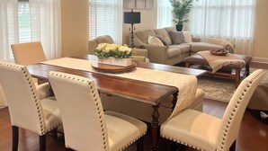 Een woonkamer met een houten eettafel, vier gestoffeerde stoelen, een bank en een plafondventilator.