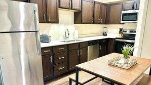 A modern kitchen with dark wooden cabinets, stainless steel appliances, and a wooden table with a plant centerpiece.