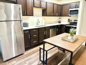 Una cocina moderna con armarios de madera oscura, electrodomésticos de acero inoxidable y una mesa de madera con un centro de mesa con planta.