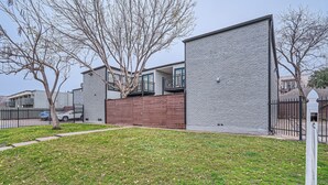 A modern building with a brick facade, a wooden deck, and a fenced yard.