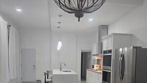 Una cocina moderna con una isla central, electrodomésticos de acero inoxidable y una lámpara decorativa.