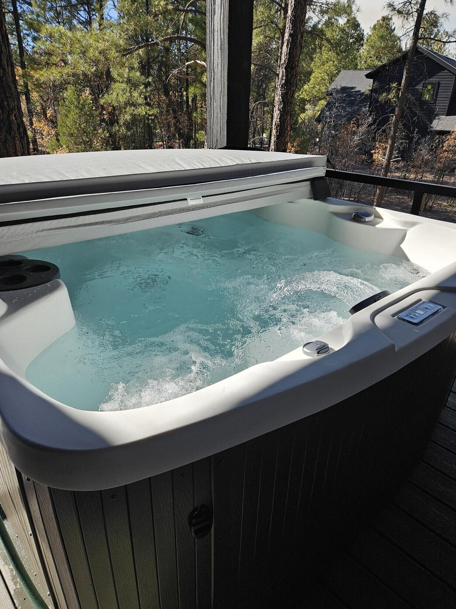 A hot tub on a wooden deck with a view of trees and a house in the background.