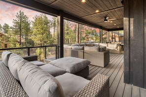 A covered outdoor seating area with wicker furniture and a view of trees and buildings. - Luxe Mountain Lodge with Hot Tub (Show Low)