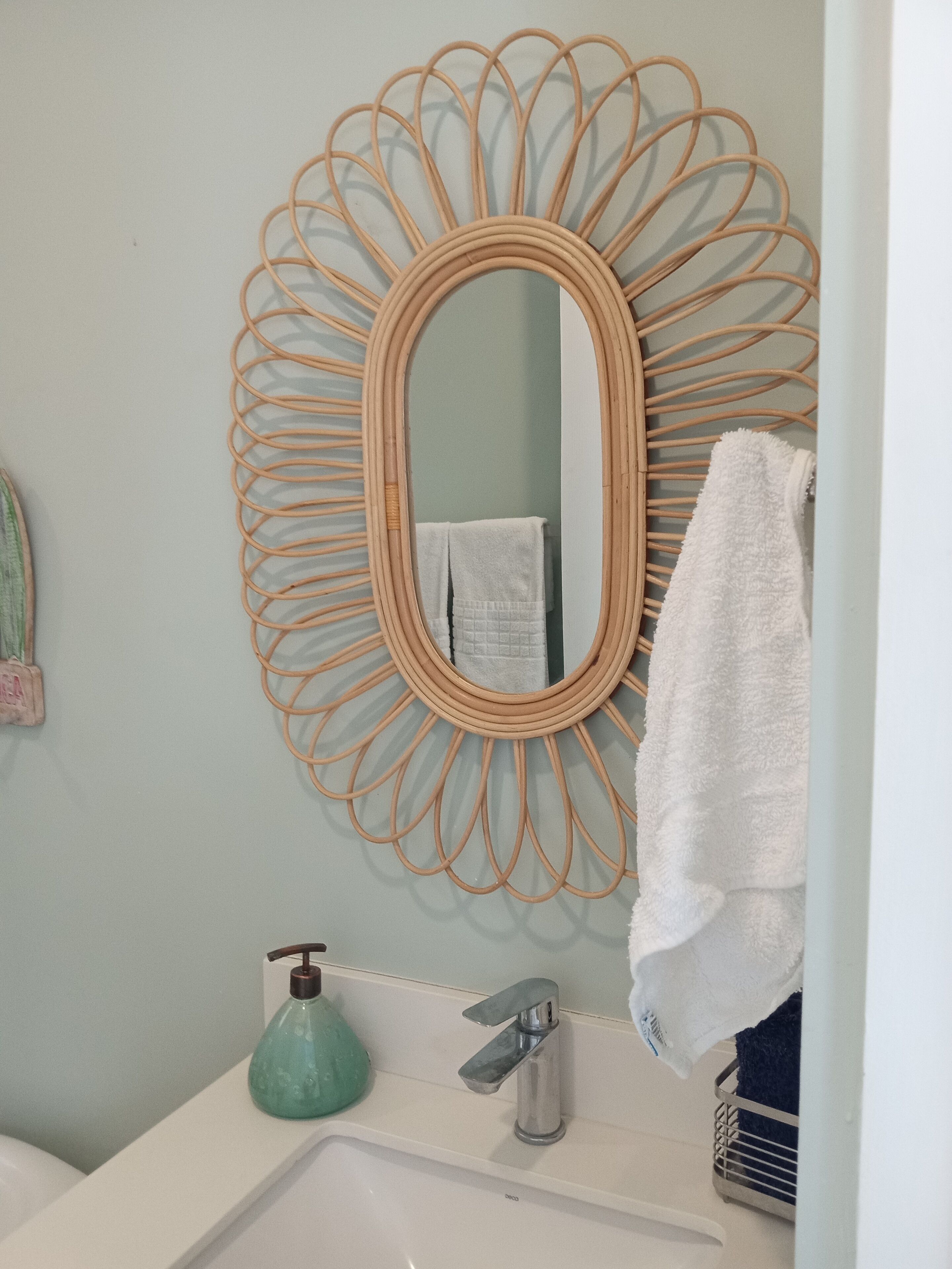 A bathroom with a round mirror, a sink, a faucet, a soap dispenser, and a towel rack.