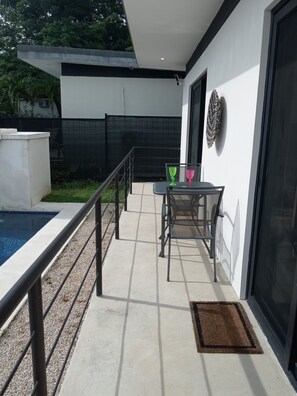 Une terrasse extérieure moderne avec une piscine, une table entourée de chaises et une porte vitrée donnant sur l’intérieur.