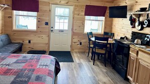 Interior acogedor de una cabaña con una cama, una mesa de comedor con sillas, una zona de cocina y una puerta con un cartel de 'No Smoking'.