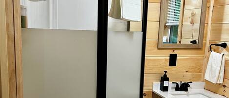 A wooden-paneled bathroom with a glass-enclosed shower, a sink with a mirror, and a wooden cabinet.
