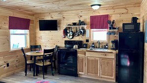 Una cocina compacta con paredes de madera, un comedor con sillas, un refrigerador negro, una estufa y un microondas.