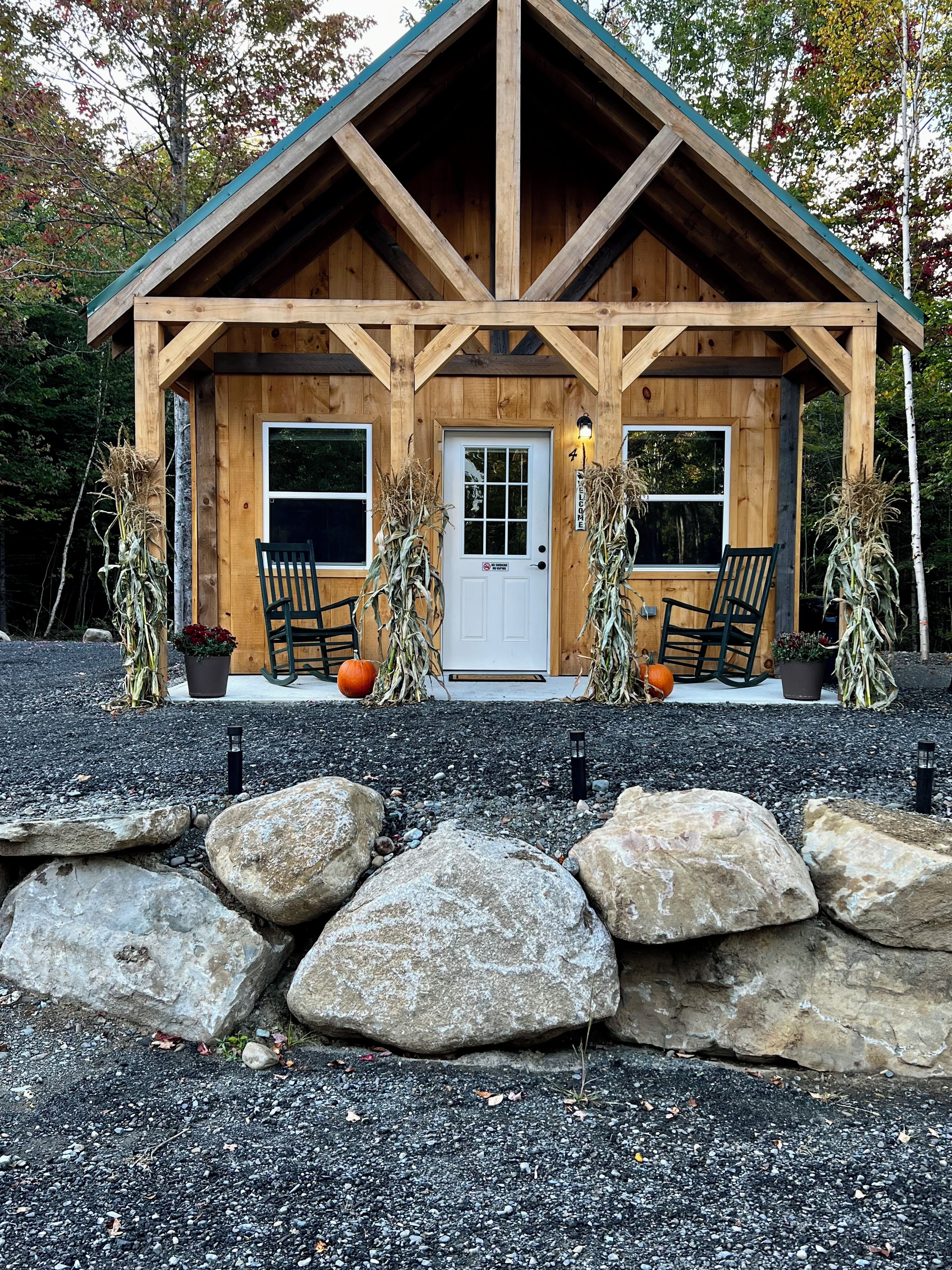 A wooden cabin with a pitched roof, two windows, a door, and a porch with two chairs.