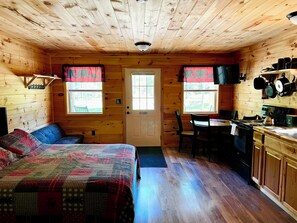 Eine Hütte mit einem Bett, einem Esstisch, Stühlen, einer Küchenzeile inklusive Herd und einer Tür mit Fenstern.