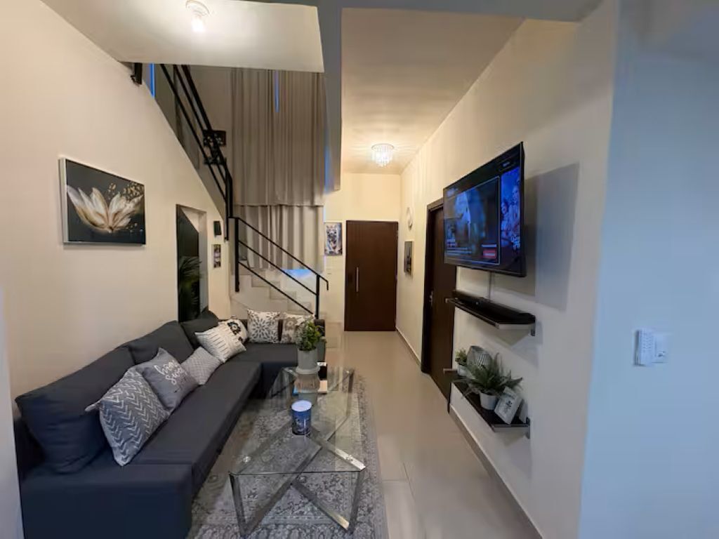 Uma sala de estar moderna com sofá, mesa de centro, TV, escada e uma porta.