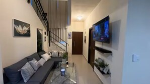 A modern living room with a sofa, coffee table, TV, staircase, and a door. - 3Bed-3Bath Villa in Beautiful Punta Cana with AC (Punta Cana)