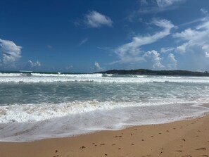 Une plage avec des vagues, une étendue de sable et une terre lointaine sous un ciel dégagé.