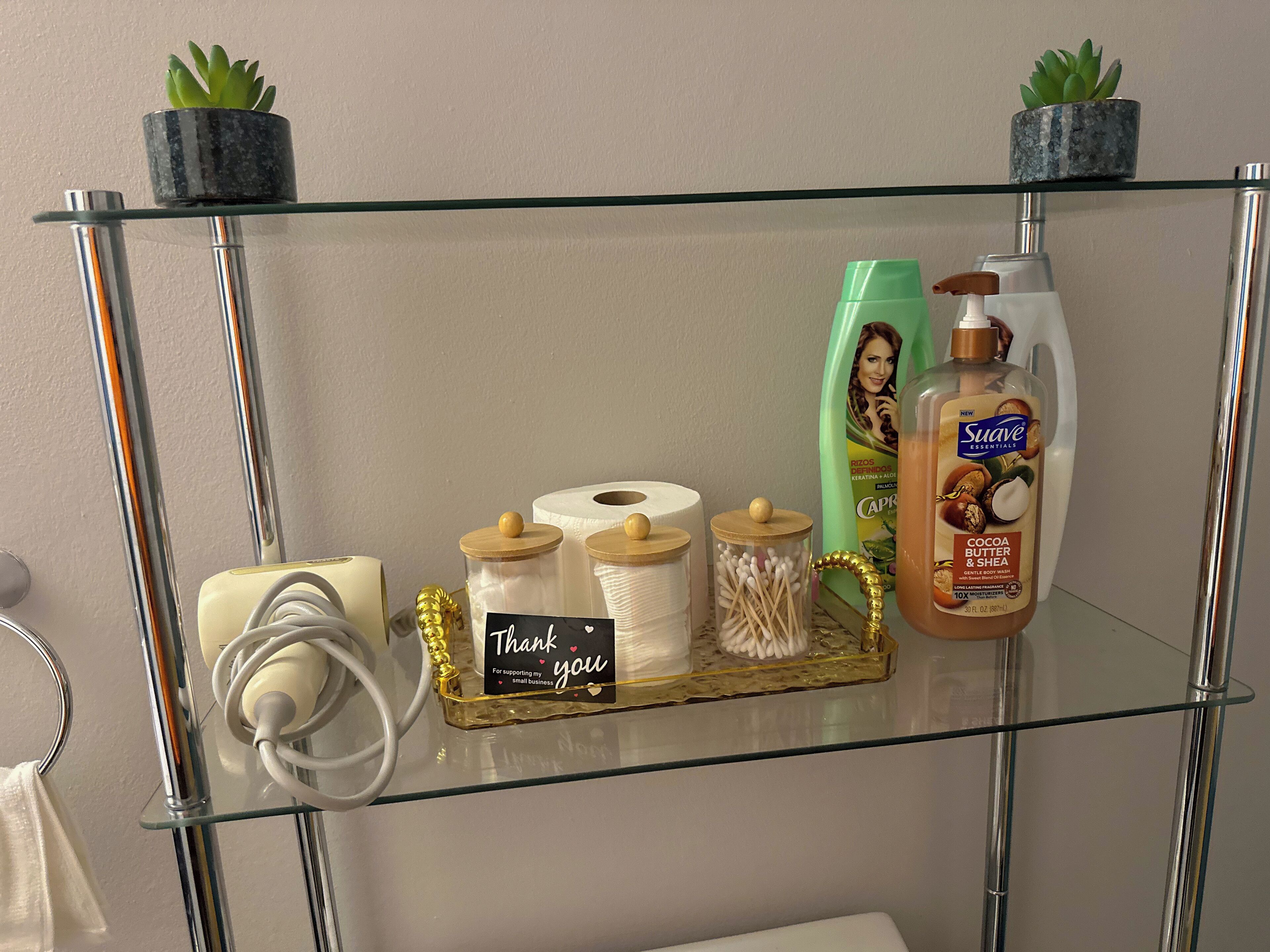 A glass shelf with toiletries, including a bottle of Suave Essentials, cotton swabs, and a thank you card.