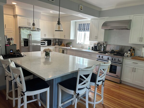 Una cocina moderna con una isla grande, armarios blancos, electrodomésticos de acero inoxidable y piso de madera.