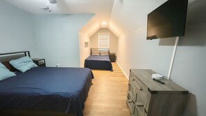 Une chambre à coucher avec un lit, une commode, un téléviseur et une fenêtre avec des stores.