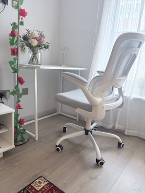A white office chair with a high backrest and armrests, positioned on a light-colored wooden floor.