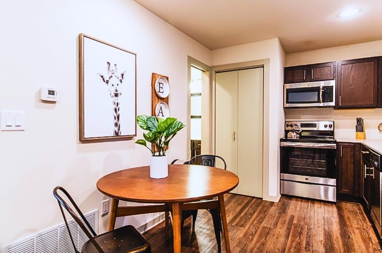 Une cuisine moderne avec des meubles en bois, des appareils en acier inoxydable, une table à manger avec des chaises et une plante en pot.