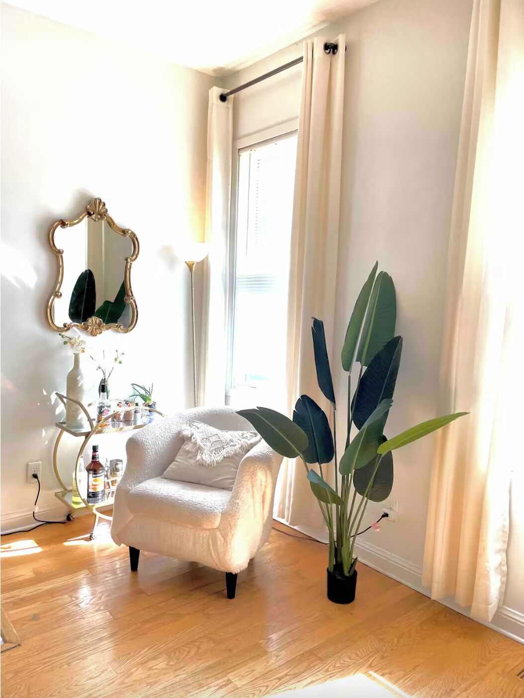 Ein gemütliches Zimmer mit einem weißen Sessel, einem großen Spiegel und einem Blumentopf.