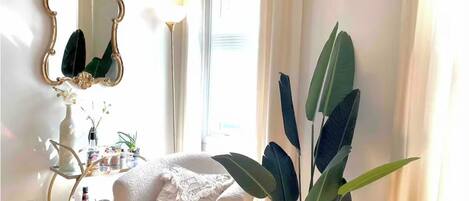 Ein gemütliches Zimmer mit einem weißen Sessel, einem großen Spiegel und einem Blumentopf.