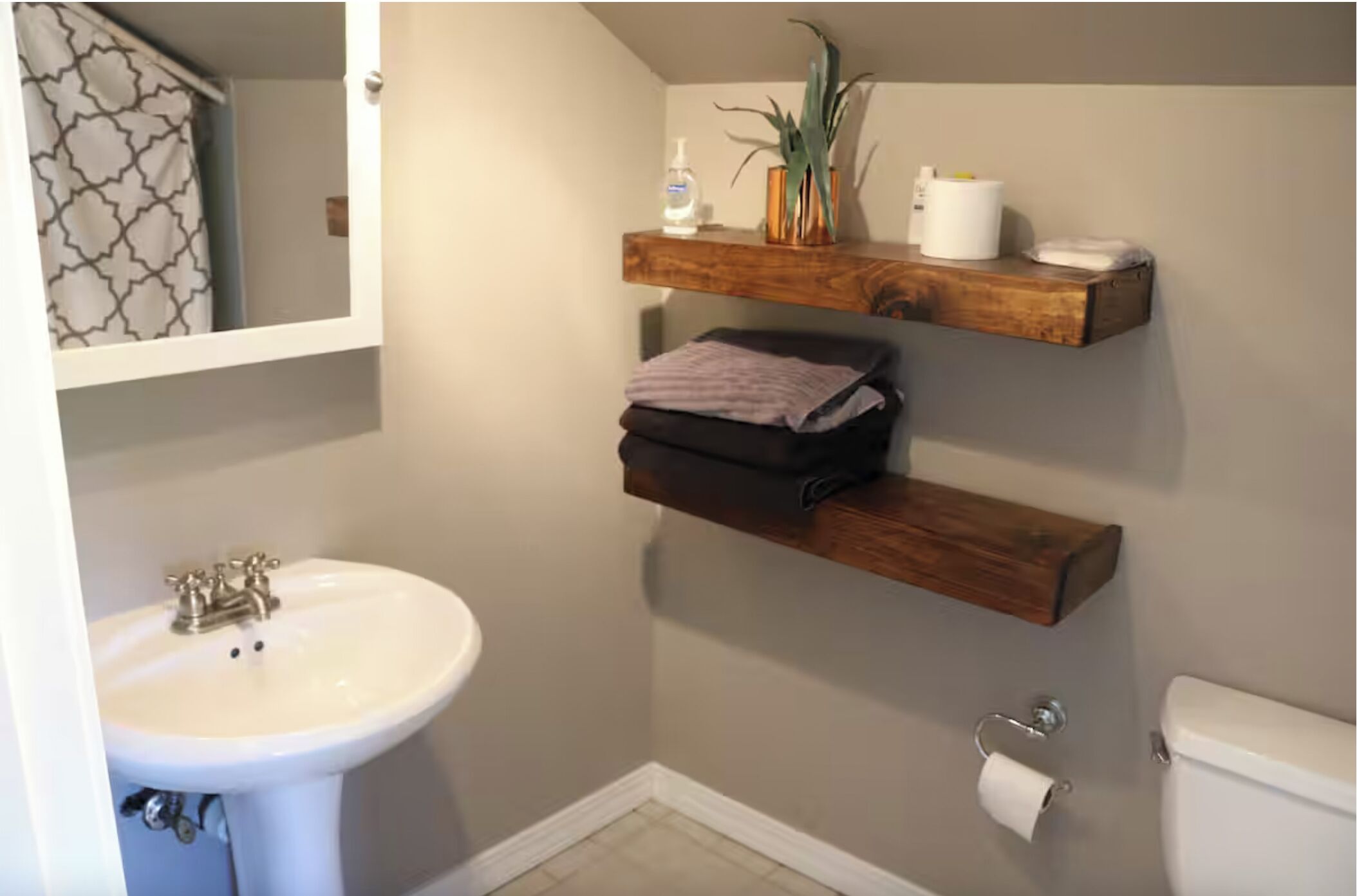 A bathroom with a white sink, a toilet, and two wooden shelves above the toilet.