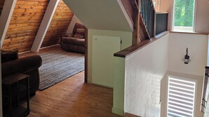 A loft-style room with a wooden ceiling, a staircase with wooden railings, a small white cabinet, and a brown leather couch. - 4-bedroom cabin in peaceful Lakeside Oregon (Lakeside)