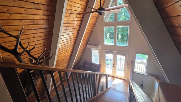 A wooden staircase with a ceiling fan, leading to a second-floor room with large windows and a view of the outdoors. - 4-bedroom cabin in peaceful Lakeside Oregon (Lakeside)