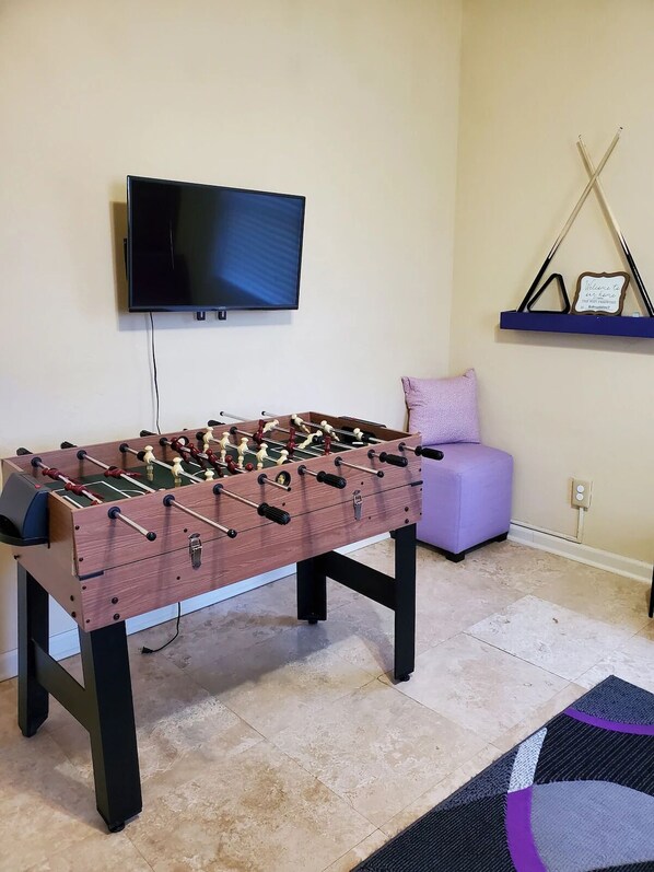A room with a foosball table, a television mounted on the wall, a purple ottoman, and a shelf with a welcome sign. - 7 rooms and 3 bathrooms NEW! (Weinböhla)
