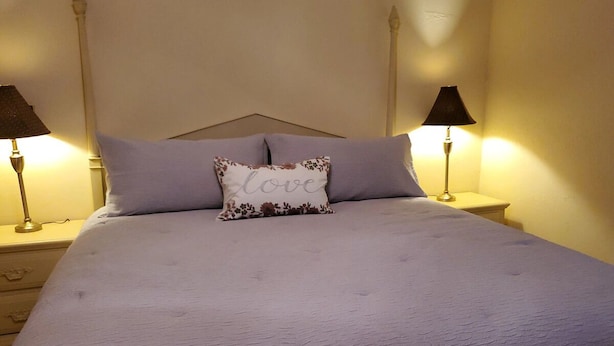 Uma cama bem arrumada com um travesseiro floral, duas luminárias de cabeceira e uma mesa de cabeceira com gavetas.