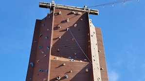 Uma parede de escalada de madeira alta com vários apoios e uma corda de segurança vermelha.