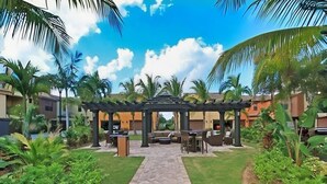 A covered outdoor seating area with a paved walkway leading to it, surrounded by palm trees and greenery. - SW FL Vacation Paradise! Minimum 1 week stay, long term renters welcome.  (Fort Myers)