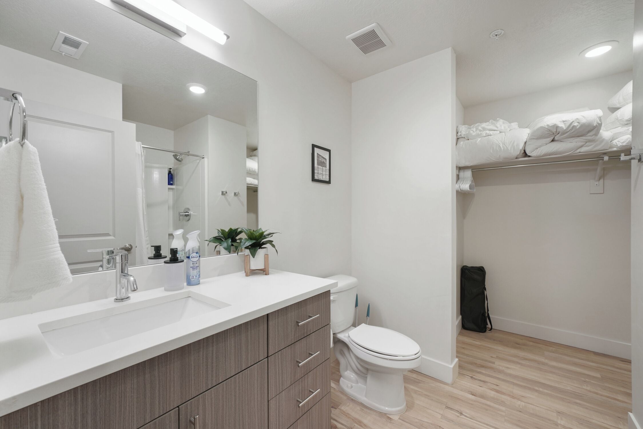 Un baño moderno con un lavamanos blanco, armarios de madera, un inodoro y una zona de ducha.