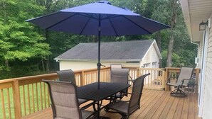 A wooden deck with a dining table and chairs, a blue umbrella, and a house in the background. - We Are…..2 miles from Beaver Stadium! (State College)