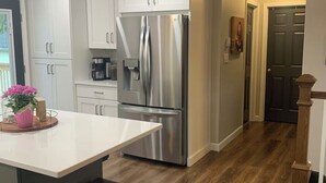 A modern kitchen with white cabinets, a stainless steel refrigerator, a wooden island with a bar stool, and a dark wooden floor. - We Are…..2 miles from Beaver Stadium! (State College)