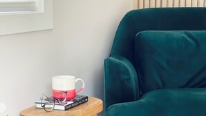 A teal armchair, a wooden stool with a mug and books, and a patterned rug. - Cozy Studio downtown Carson, near Tahoe/Reno (Carson City)