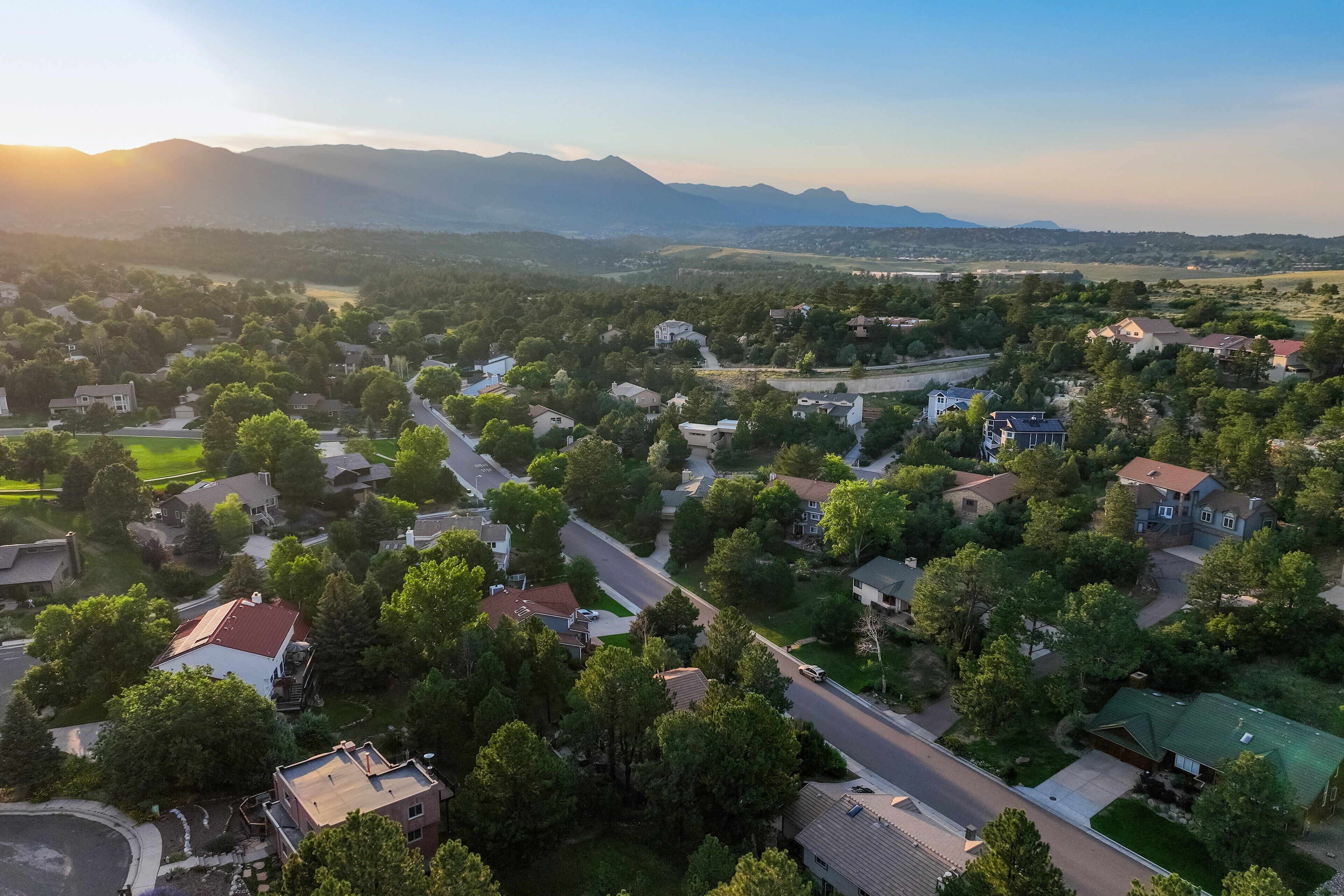 An aerial view of a residential area with houses, roads, and surrounding greenery.