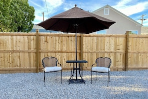 Une terrasse avec une table et deux chaises, une clôture en bois et une maison en arrière-plan.