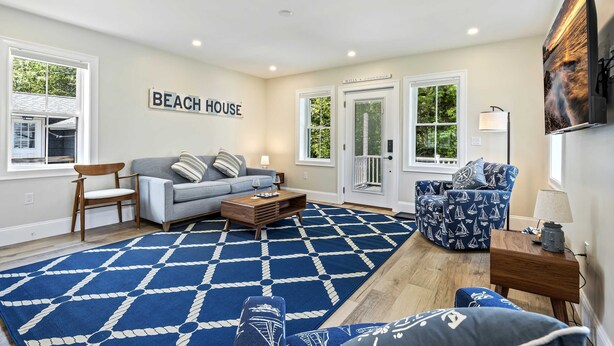 Ein Wohnzimmer mit einem blauen Teppich mit Muster, einem grauen Sofa, einem blauen Ohrensessel mit Muster und einem Holztisch.