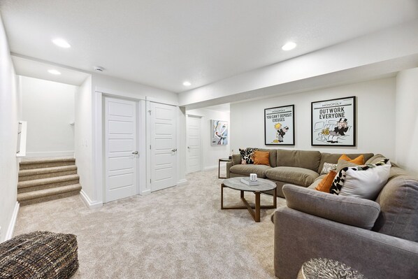 A living room with a grey sofa, a coffee table, and a staircase leading to a door. - Peaceful, private & Fun near Old Town, Breweries, bike trails & hot tub (Fort Collins)