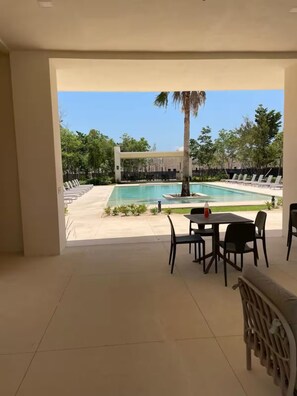 A pool area with lounge chairs and a table, surrounded by greenery and a clear sky. -  Cancun Breeze3-bedroom house in terrific Quintana Roo , close to Xcaret parks (quintana roo)