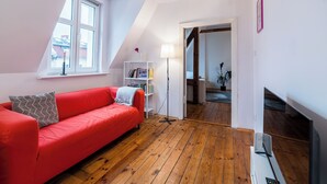 Un apartamento loft moderno con sofá rojo, suelo de madera, radiador blanco y tragaluces.