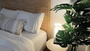 A neatly made bed with white linens and patterned pillows, a wooden headboard, and a bedside table with a lamp and a book. - Chic Absolute - Your Next Urban Oasis (Atlanta)