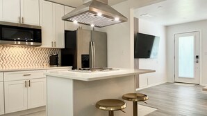 A modern kitchen with white cabinetry, a stainless steel microwave, a coffee machine, and a large island with stools. - Chic Absolute - Your Next Urban Oasis (Atlanta)