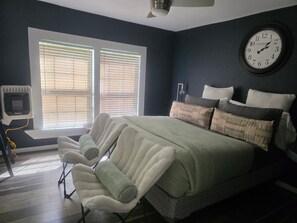 A bedroom with a bed, pillows, a clock, and a window with blinds.