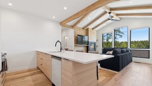 A modern kitchen with a central island, wooden beams, and large windows offering a view of the outdoors. - Newly built two bedroom rental with Blanchard Lake access in Whitefish! (Whitefish)