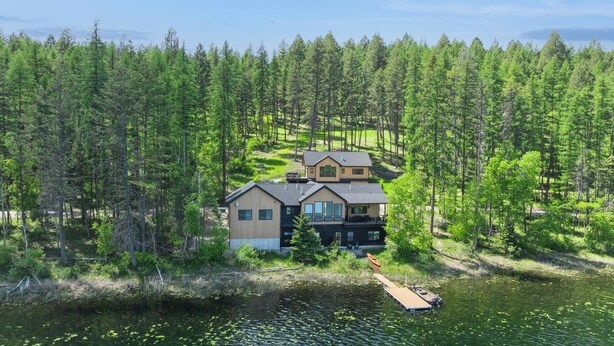 A two-story house with a dock extending into a lake, surrounded by dense forest. - Newly built two bedroom rental with Blanchard Lake access in Whitefish! (Whitefish)