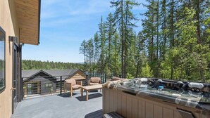 A wooden deck with outdoor seating and a hot tub, overlooking a forested area. - Newly built two bedroom rental with Blanchard Lake access in Whitefish! (Whitefish)
